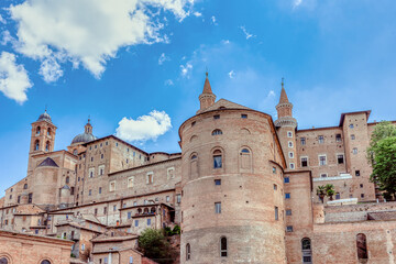 A stunning view of Urbino's cityscape showcasing the impressive Palazzo Ducale under a bright blue sky. Palazzo Ducale Castle of the Dukes of Urbino, Italy