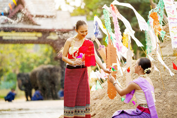 Obraz premium Beautiful Thai women in the Thai traditional dress help stick the triangular flag on the sand pile in temple in Songkran festival.
