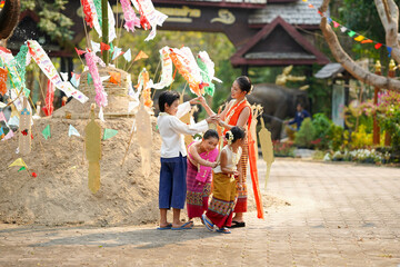 Naklejka premium Group of Thai children's with beautiful Thai young woman and in the Thai traditional dress playing human cave train on outdoor pile of sand in temple at the Songkran festival.