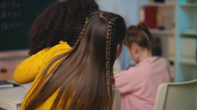 Two multiethnic female friends whispering about their classmate behind her back