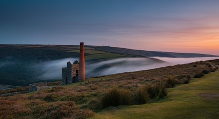 Old chimney and ruins on grassy hillside during sunset with misty valley