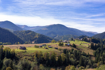 Breathtaking Autumn Landscape of Rolling Hills with Traditional Houses Nestled Among the Lush Greenery and Majestic Mountains Under a Clear Blue Sky