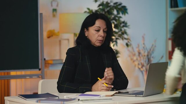 Tired teacher struggling to work while noisy pupils run around in the classroom