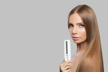 Nice brunette lady with straight hair holding straightening iron on white background. Female...