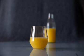 glass orange juice the table. In background, not full bottle juice out of focus.