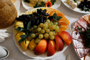 Various fruits are beautifully arranged on the plate: grapes (green and dark), sliced ​​orange, apple and peach.