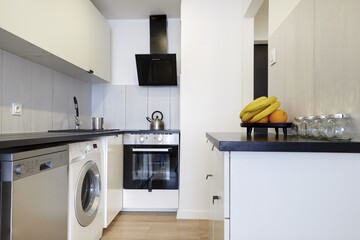 Kuchnia w nowoczesnym apartamencie w jasnym kolorze  z czarnym blatem,  owoce