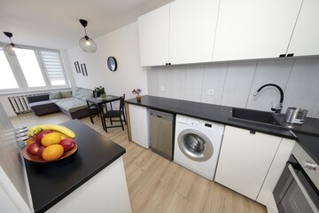 Kuchnia w nowoczesnym apartamencie w jasnym kolorze  z czarnym blatem,  owoce