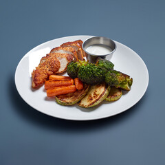 Grilled Chicken with Roasted Vegetables and Sauce on White Plate Against Blue Background