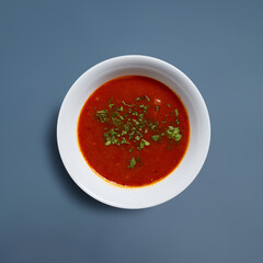 Spicy Tomato Soup with Herbs in White Bowl Against Blue Background