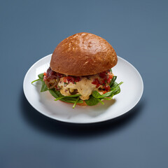 Spicy Burger with Melted Cheese and Spinach on White Plate Against Blue Background
