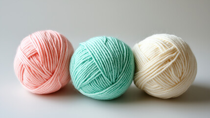 Three yarn balls in light pink, mint, and cream on smooth surface
