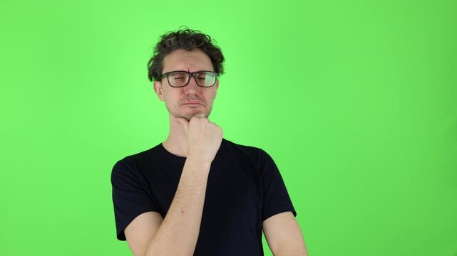 thoughtful puzzled man in who looks around touching chin and weighs pros cons of offer. isolated on green studio background, chromakey. concept - brainstorm, reasoning, analysis, fake news, good idea.
