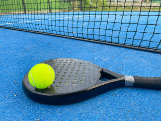 Yelllow tennis ball on black padel racket on blue turf court. Racquet sport, fun game experience concepts