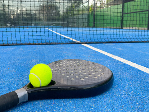 Tennis ball on black padel racket on blue turf court. Racquet sport, fun game experience concepts - Powered by Adobe