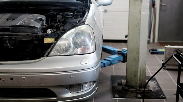 Lifting a silver car up in the air on a two post lift so a mechanic can work underneath it in a garage. 4k static shot.