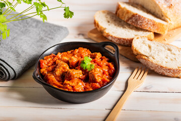 Pork in tomato sauce, a traditional dish from Andalusia, accompanied by bread for dipping in the sauce, close-up.
