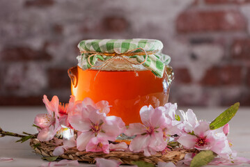 Glass jar with bee honey surrounded by almond blossoms, close-up.