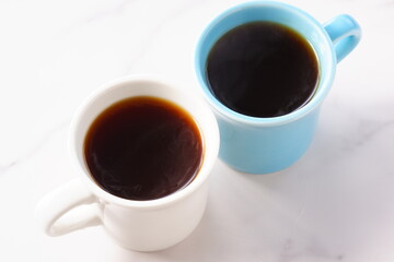 淹れたてのコーヒーが入ったふたつのマグカップで、ふたりがコーヒーを飲みながら、打ち合わせをしているイメージ
