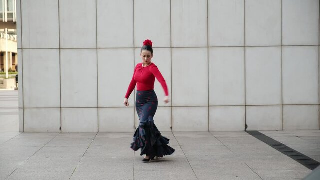 Young woman dancing flamenco with red shirt and bata de cola in front of a modern building
