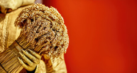 A golden figure holds a bouquet of wheat against a vibrant red backdrop at an artistic exhibition showcasing farm life