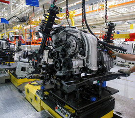 Assembly workers install car engines on production line in a modern automotive plant during daytime operations
