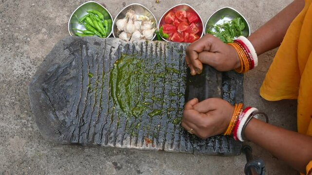 Grinding coriander chutney on stone grinder.
Indian Woman hands grinding fresh coriander leaves with garlic, chillies, tomato and Salt on stone grinder. Traditional way of sauce making in India.