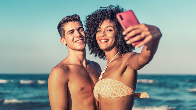 Interracial couple taking a selfie at the beach on a sunny day