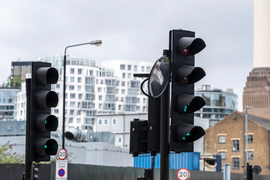 Traffic lights in an urban street with industrial buildings and a cloudy sky in the background.