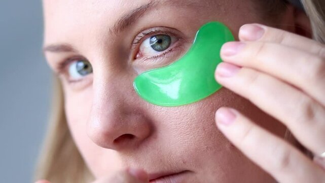 Close up of a caucasian millennial woman with no makeup using green gel moisturizing patches under her eyes. Skincare routine on natural at home . High quality FullHD footage