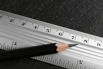 Metal ruler and pencil on black table, top view