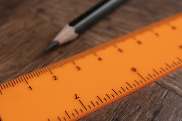 Orange ruler and pencil on wooden table, closeup