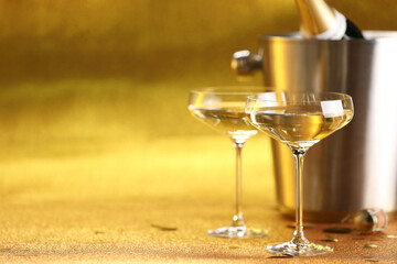Champagne in glasses and ice bucket with bottle on golden background. Space for text