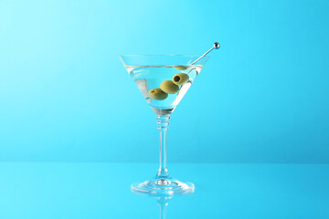 Martini cocktail with olives in glass on light blue background