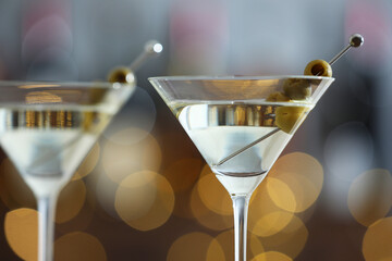Martini cocktail with olives in glasses on blurred background, closeup. Bokeh effect