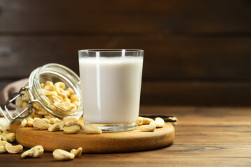 Fresh cashew milk in glass and nuts on wooden table, space for text