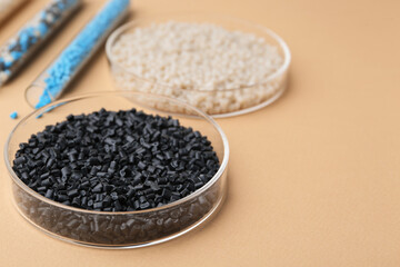 Colorful plastic granules in petri dishes and test tubes on beige background, closeup. Space for text