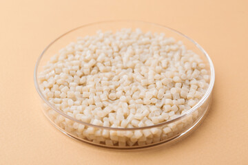 Plastic granules in petri dish on beige background, closeup