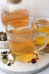 Delicious herbal tea with honey and dry leaves on white table, closeup