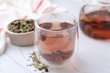 Delicious herbal tea and dry leaves on white table, closeup
