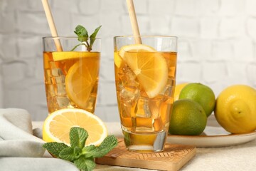 Refreshing iced tea with drinking straws, mint, lemon and lime on light table against grey background, closeup