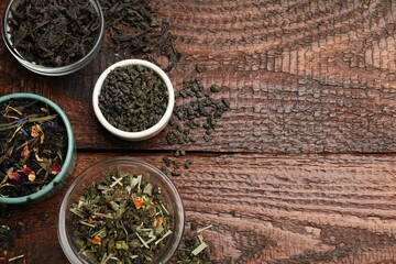 Different dry tea leaves in bowl on wooden table, flat lay. Space for text