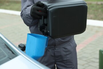 Man pouring fuel from canister into funnel outdoors, closeup