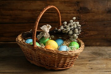 Beautiful decorated Easter eggs in wicker basket and willow branches on wooden table