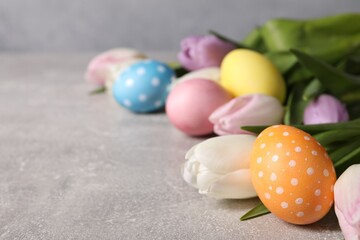 Easter eggs and beautiful tulips on grey table, closeup. Space for text