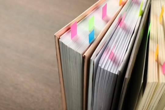 Books with colorful tabs on brown table, closeup. Space for text