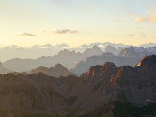 Majestic Dolomites during sunrise, mist softening mountain ridges, creating ethereal depth. Light highlights rugged peaks, warm golden glow enhances tranquil landscape. Adventure, nature, scenic. Trav