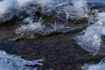mountain river with pebbles at the bottom covered with ice with patterns