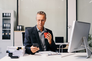 Fototapeta premium Mature male businessman using mobile phone play social and enjoys a coffee in office.