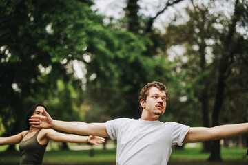 Fototapeta premium Students participate in an outdoor fitness class with their instructor, stretching arms and focusing on health. The scene captures a sense of camaraderie and well-being in a lush, green park setting.